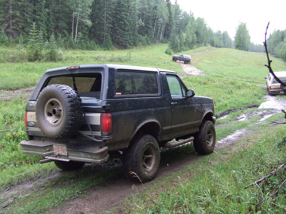 Black 1995 Ford Bronco with spare tire on rear, driving on a muddy trail