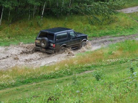 1995 Ford Bronco - A black Ford Bronco navigates a muddy trail with trees in the background.