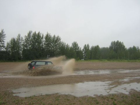 1995 Ford Bronco - A dark SUV navigates through a muddy field, creating large splashes.