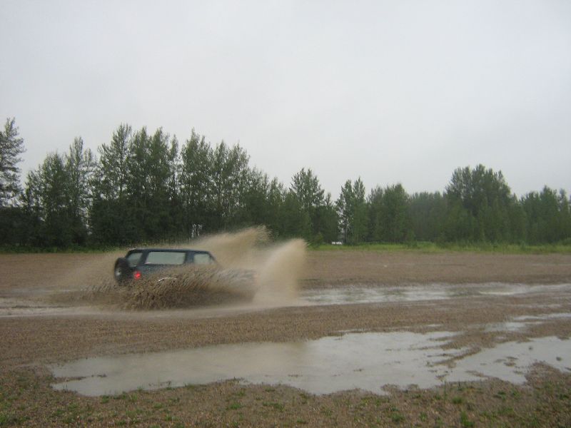 Dark SUV kicking up mud splashes while driving through a muddy field