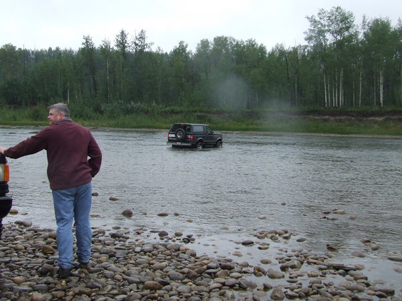 1995 Ford Bronco driving through a river with a man standing on the shore