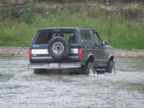 1995 Ford Bronco - This Ford Bronco is driving through a shallow body of water with trees in the background.