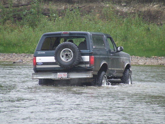 Dark green Ford Bronco with a rear-mounted spare tire driving through water