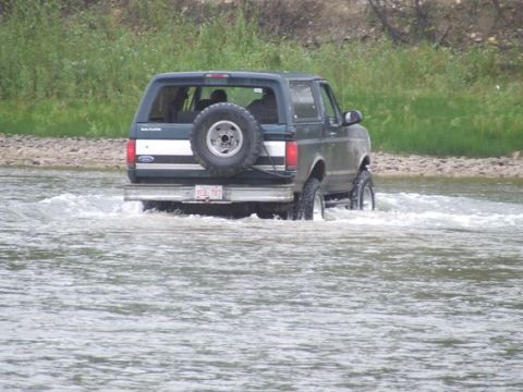 1995 Ford Bronco - A 1995 Ford Bronco navigates through a shallow body of water, kicking up spray.