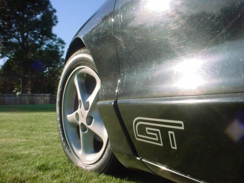 1994 Ford Probe - A close-up shot of a car's side panel, a GT badge and a wheel, with visible scratches on the paint.