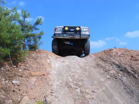 1993 Ford Bronco - This 1993 Ford Bronco is captured from the front as it ascends a steep dirt incline under a bright blue sky.