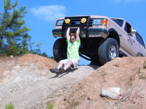 1993 Ford Bronco - Man hangs from the front bumper of a lifted 1993 Ford Bronco during an off-road excursion.