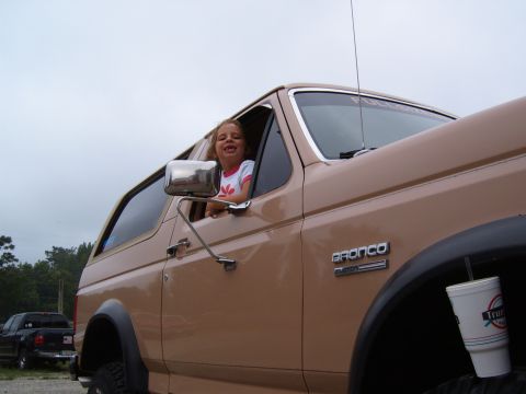 1993 Ford Bronco - A young girl smiles from the driver's side window of a tan Ford Bronco, with another vehicle visible in the background.