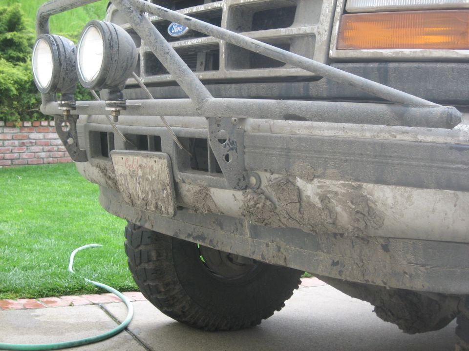 Front bumper, grille, and headlights of a muddy Ford truck with a brush guard