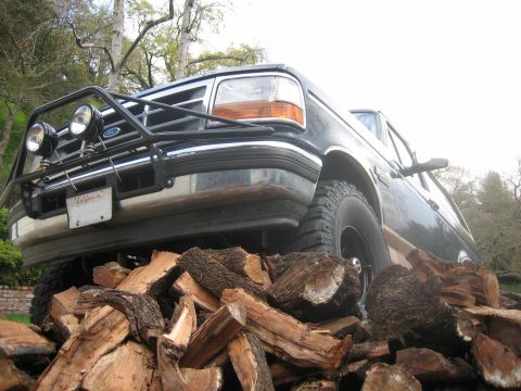 1995 Ford Bronco - A dark green Ford Bronco is positioned with its tires resting on a pile of firewood.