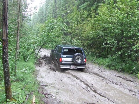1988 Ford Bronco - Ford Bronco navigates a muddy trail in a dense forest environment.