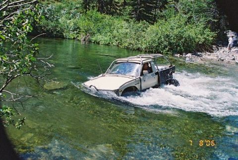 1966 Jeep CJ5 - A white pickup truck navigates a shallow river, kicking up water as it moves forward.