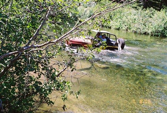 Red and yellow off-road vehicle with two people driving through a river