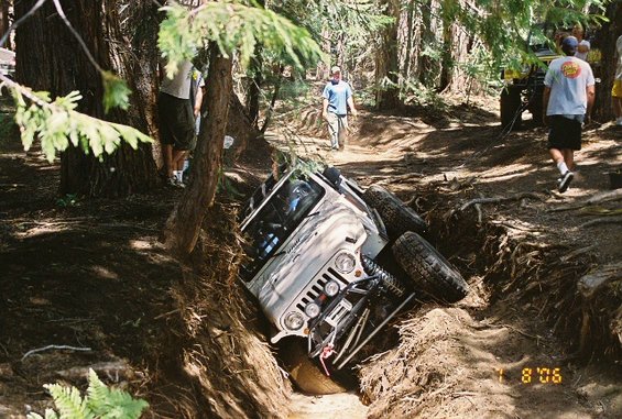 White Jeep tilted in a ditch with people around. Another Jeep is visible in the background