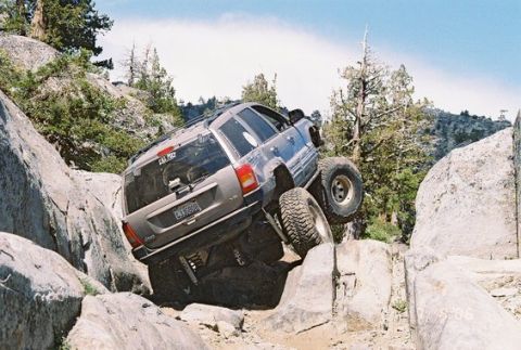 1966 Jeep CJ5 - A Jeep Grand Cherokee is shown off-roading on a challenging rocky terrain with one wheel in the air.