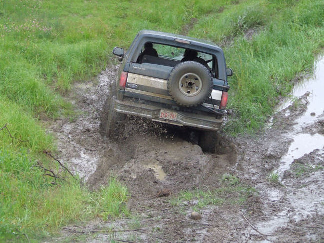 1988 Ford Bronco navigating a muddy trail, rear view with spare tire mounted