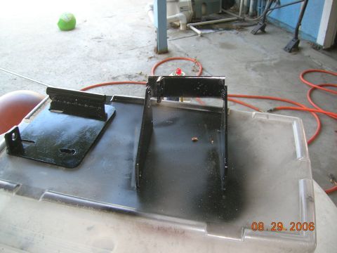 1985 Ford Bronco - A black metal bracket assembly is shown on a clear plastic bin, with an orange hose in the background.