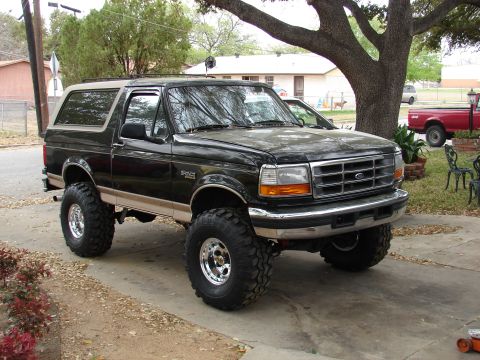 1996 Ford Bronco - This lifted black Ford Bronco is parked in a driveway with a large tree overhead.