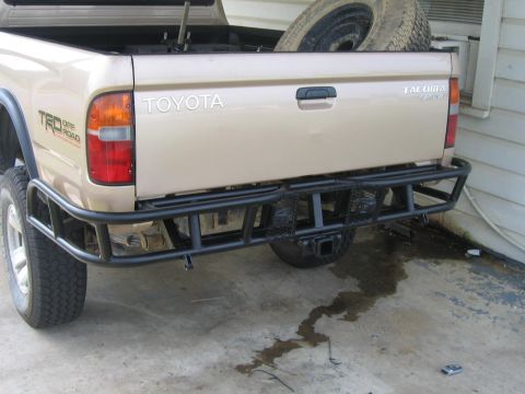 1999 Toyota Tacoma - The rear of a tan Toyota Tacoma pickup truck is shown with a custom heavy-duty bumper and a spare tire in the bed.