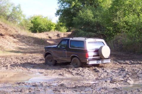 1996 Ford Bronco - A Ford Bronco navigates a muddy trail, kicking up dirt and water.