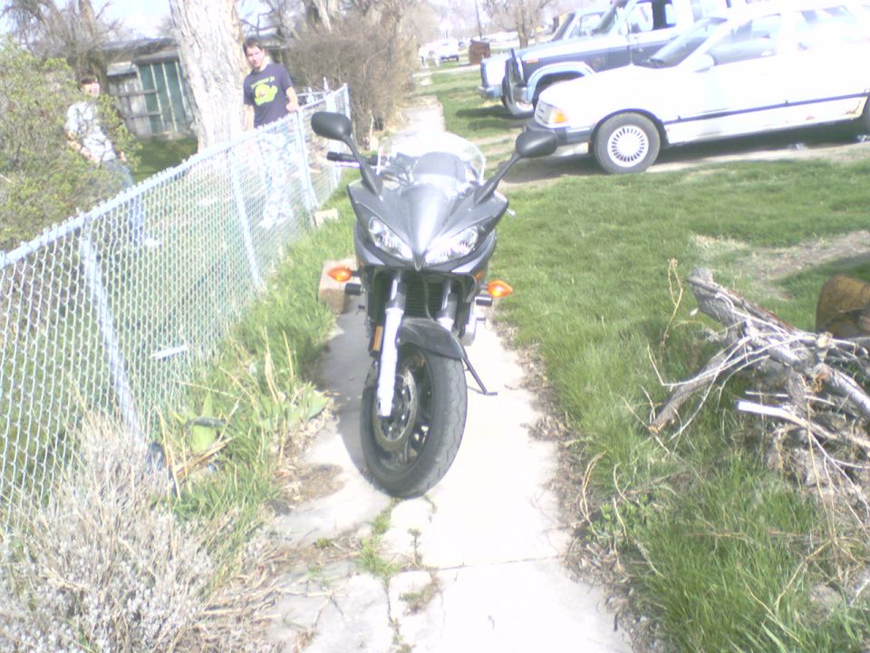 Front view of a gray faired sport motorcycle parked on a sidewalk next to a chain-link fence