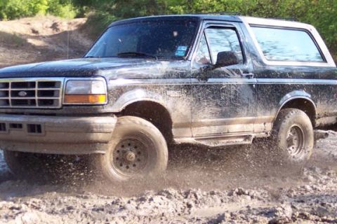 1996 Ford Bronco - This Ford Bronco is navigating a challenging muddy terrain, with water and dirt splashing around its tires.