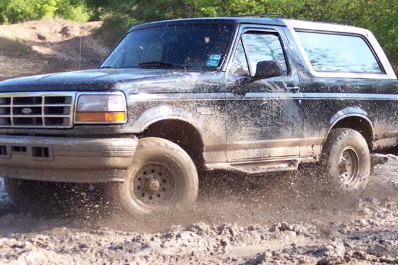 Muddy black Ford Bronco driving off-road, kicking up dirt