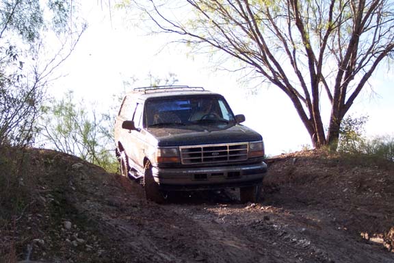 1996 Ford Bronco driving up a dirt incline with trees overhead