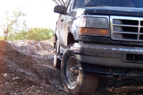 1996 Ford Bronco - A muddy black Ford Bronco navigates a treacherous dirt path.