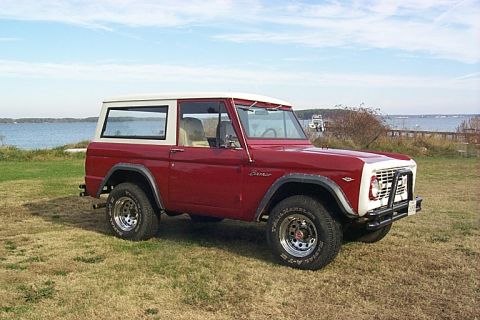 1968 Ford Bronco - This 1968 Ford Bronco features a red body with a white hardtop and is parked outdoors near a body of water.