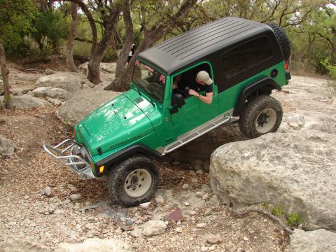 1996 Ford Bronco - A green Jeep Wrangler Rubicon navigates a rocky trail, demonstrating its off-road capabilities.