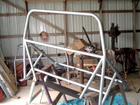 1984 Ford Bronco - A silver roll cage is assembled and supported by wooden sawhorses in a cluttered garage setting.