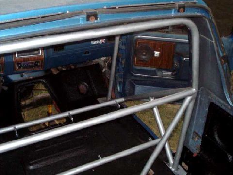 1984 Ford Bronco - The interior of a blue vehicle shows a roll cage and wood-grain trim on the dashboard.