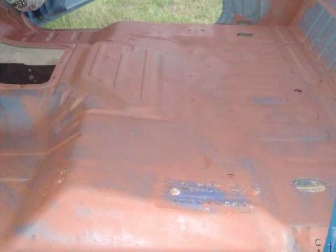 1984 Ford Bronco - The interior floor pan of a vehicle, showing areas of red primer and some blue paint.