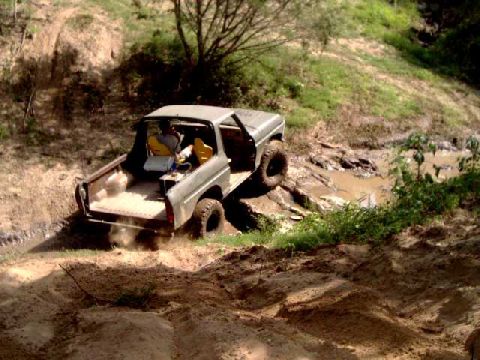 1984 Ford Bronco - An off-road vehicle navigates a challenging muddy terrain with steep inclines.