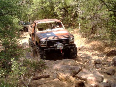 1984 Ford Bronco - Two off-road vehicles navigate a challenging rocky path through a wooded area.