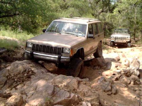 1984 Ford Bronco - Two SUVs navigate a rocky off-road trail, with the lead vehicle tackling a challenging ascent.