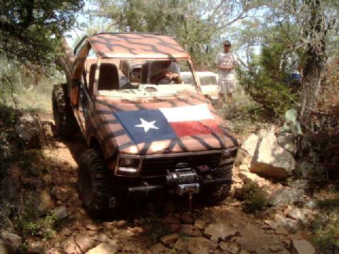 1984 Ford Bronco - A heavily modified off-road vehicle navigates a rocky trail, with a Texas flag painted on its hood.