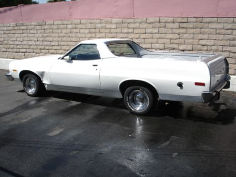 1973 Ford Ranchero - This white pickup truck has a dented front fender and is parked on a wet surface.