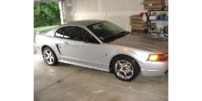 1998 Ford Taurus - A silver Ford Mustang is parked inside a garage, showing its front and side profile.