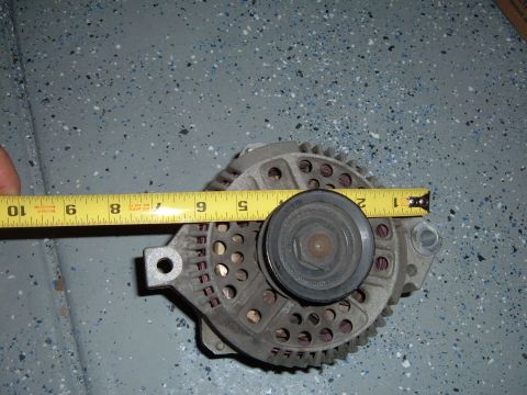 1993 Ford Bronco - An alternator is measured with a tape measure, indicating its size. The registry claims it is from a 1993 Ford Bronco.
