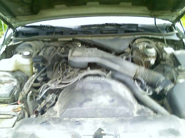 Engine bay with various hoses and components, dusty and worn. Water reservoir visible on the left