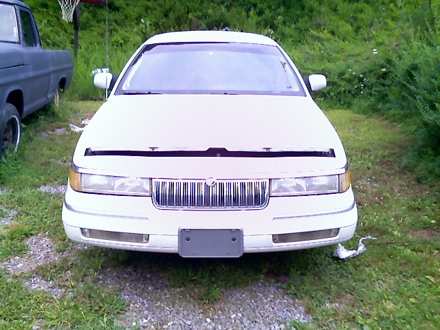 Front view of a white sedan with hood open and a chrome grille
