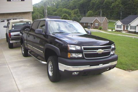 1995 Ford Bronco - A Ford Bronco with a spare tire mounted on the back is parked behind a black pickup truck.
