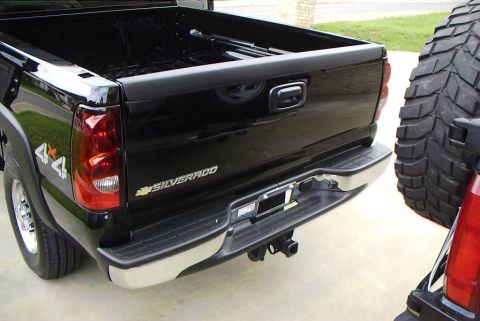 1995 Ford Bronco - The rear of a black Chevrolet Silverado pickup truck is visible, with a large off-road spare tire parked close by.