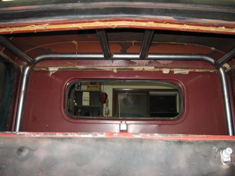 1977 Ford F-150 - The interior of a truck cab shows a roll cage and a rear window with a view into a workshop.