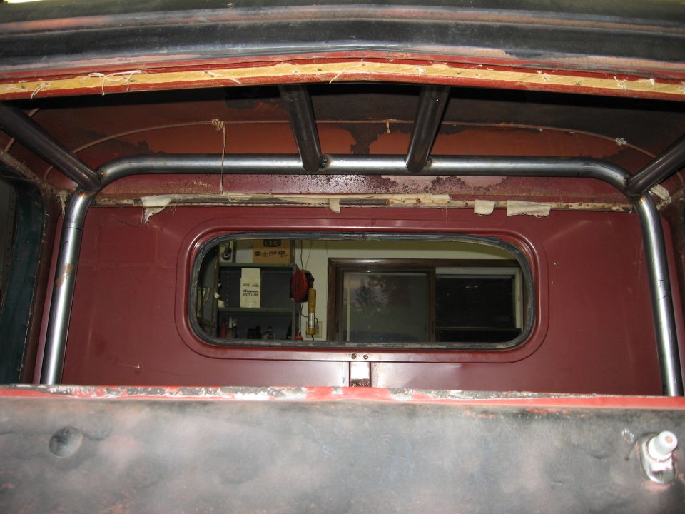 Red truck interior with a roll cage and a rear window showing a workshop
