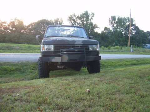 1988 Ford Bronco - This Ford Bronco has a camouflage paint job and a heavy-duty front bumper, parked on the side of a road.