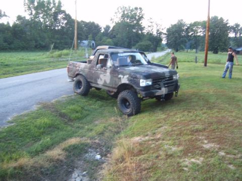 1988 Ford Bronco - Camouflaged Ford Bronco parked off the side of a rural road with two people standing nearby.