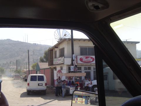1985 Ford Ranger - A white van is parked on a dusty road in front of a building with a satellite dish.